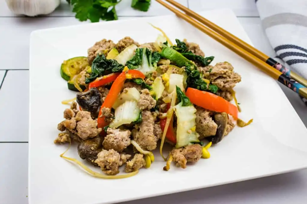 spicy keto pork stir fry on a square plate with chopsticks