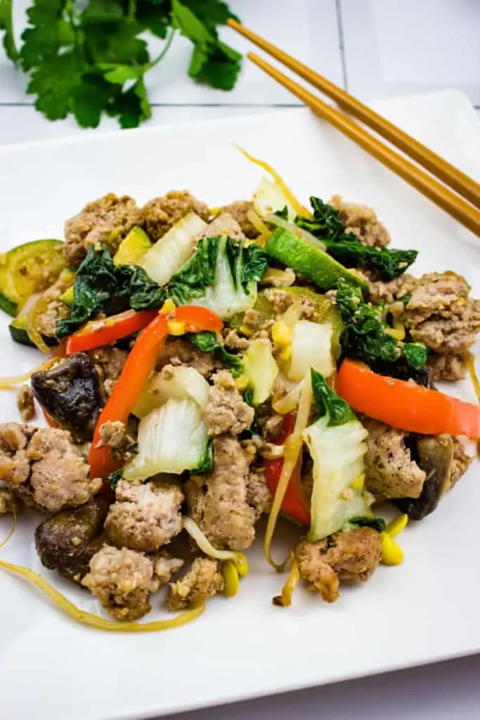 spicy keto pork stir fry with vegetables on a white square plate with chopsticks