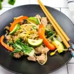 spicy keto pork stir fry with vegetables on a black plate with chopsticks