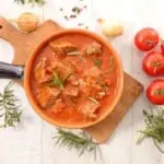 Keto Beef Goulash with sauerkraut in a bowl with tomatoes in background