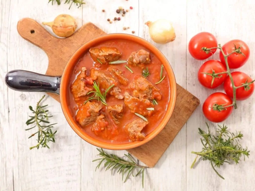 beef keto goulash with sauerkraut in a bowl with tomatoes in background