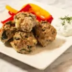 Greek meatballs on a plate with tzatziki and sauteed peppers.