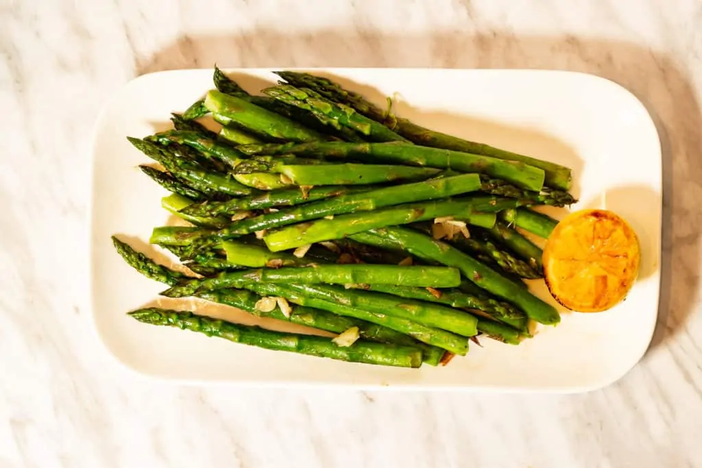 Keto pan-roasted asparagus spears on a plate with caramelized lemon.