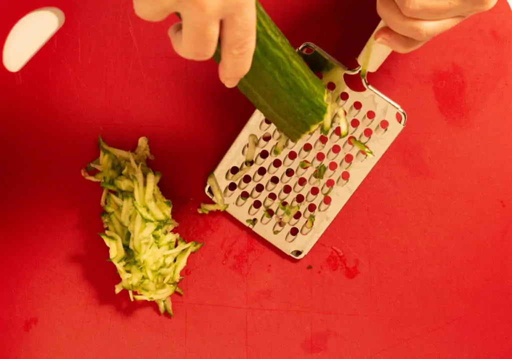 Grating an English cucumber with a cheese grater.
