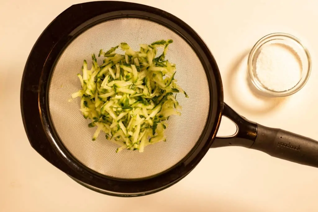 Salted shredded cucumber in a sieve.