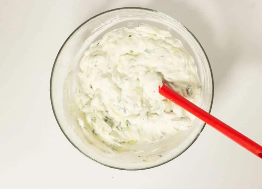 Finished tzatziki in a mixing bowl with red spatula.