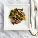 Keto and low-carb sausage & kale in a white wine garlic sauce with peppers on a square plate.