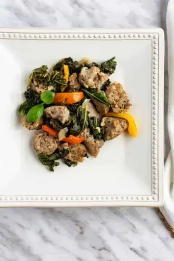 Keto and low-carb sausage & kale in a white wine garlic sauce with peppers on a square plate.