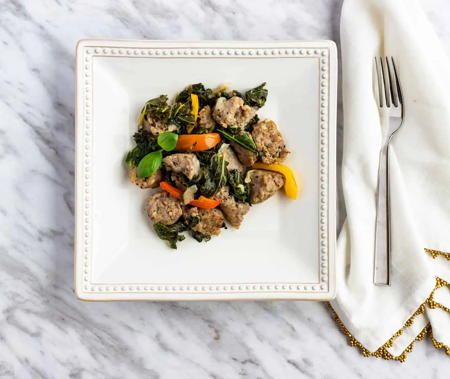 Keto and low-carb sausage & kale in a white wine garlic sauce with peppers on a square plate.