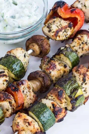 three keto and low-carb lemon-oregano chicken kabobs on a plate with a side of tzatziki