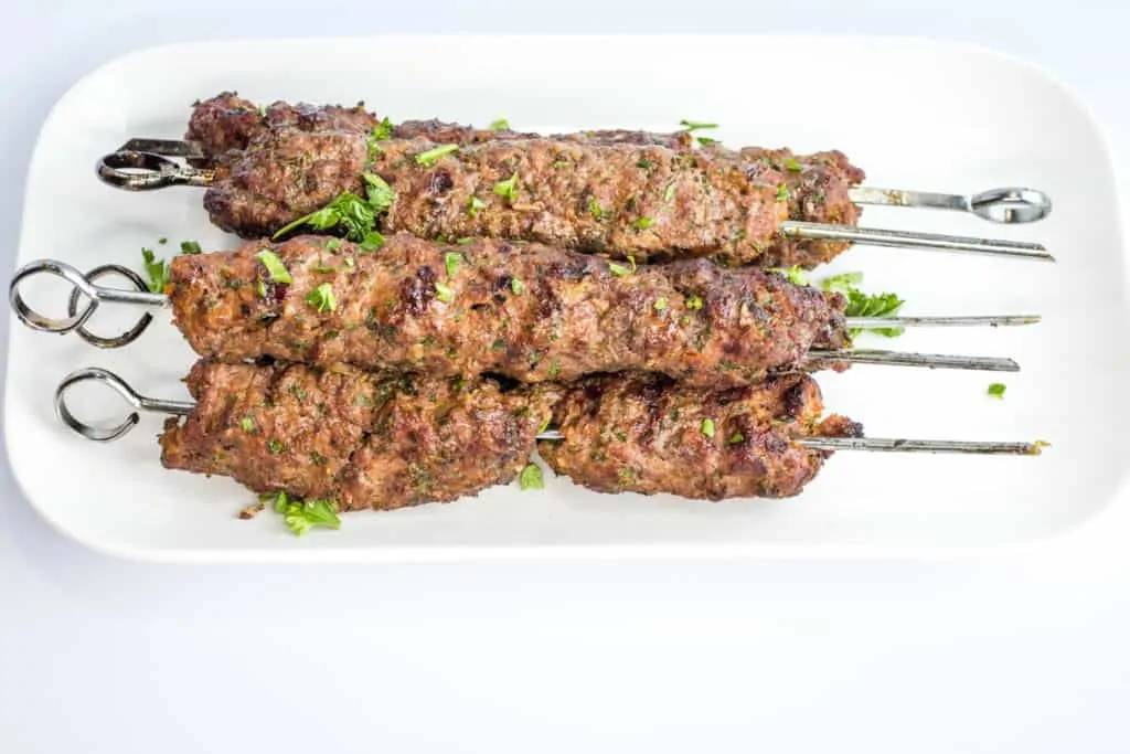 five skewers of grilled low-carb/keto kefta beef kabobs on a white plate