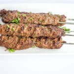 five skewers of grilled low-carb/keto kefta beef kabobs on a white plate