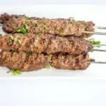 five skewers of grilled low-carb/keto kefta beef kabobs on a white plate