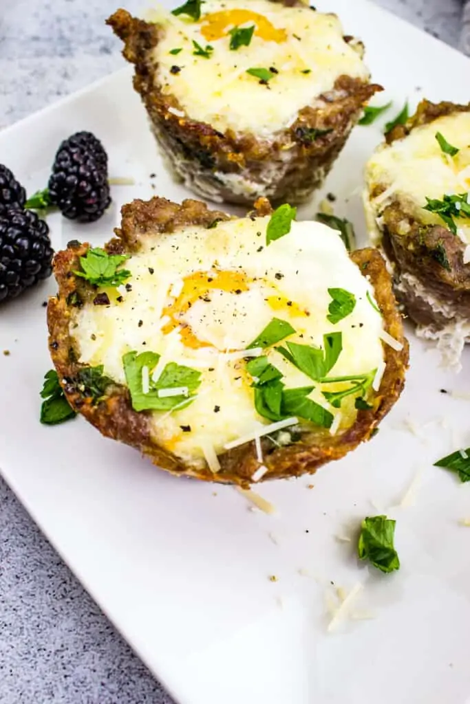 sausage and egg cups on a white plate with blackberries 