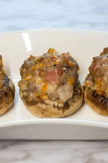 three keto and low carb bacon, sausage and cheese stuffed mushroom caps on a plate