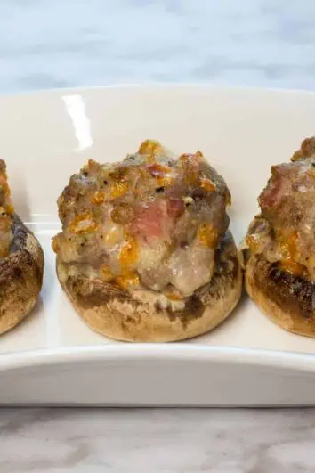 Three keto and low carb bacon, sausage and cheese stuffed mushroom caps on a plate