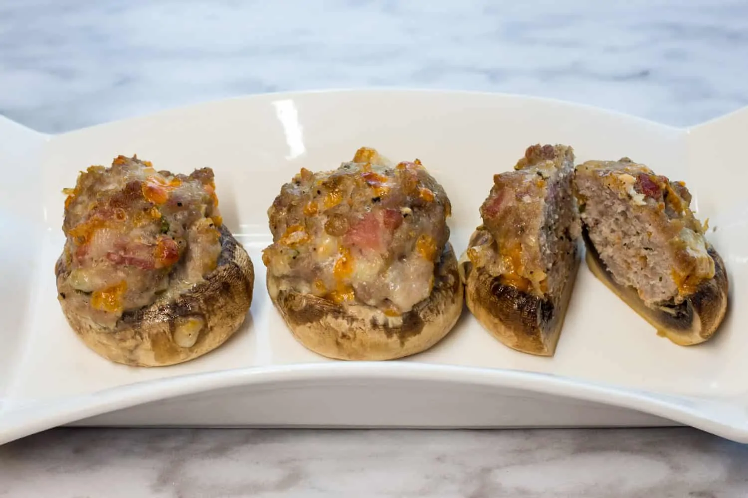 Three keto and low carb bacon, sausage and cheese stuffed mushroom caps on a plate