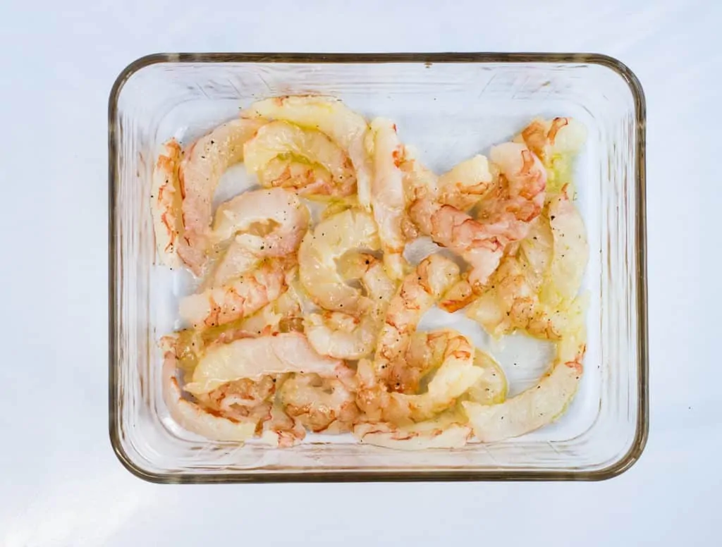 raw shrimp dressed with olive oil, salt and pepper in a glass roasting dish