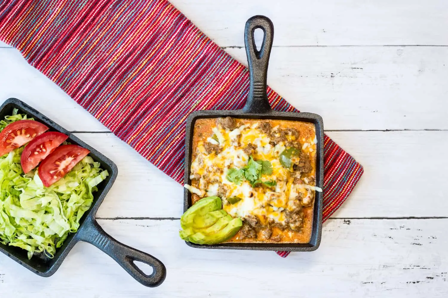 Tex-Mex Beef Casserole in a small square cast iron serving dish with another dish of lettuce and tomato on the side.