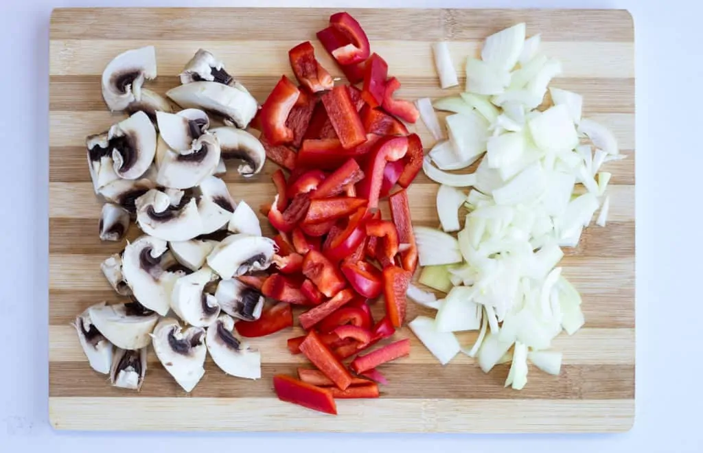 chopped mushrooms, onions, and peppers on a cutting board