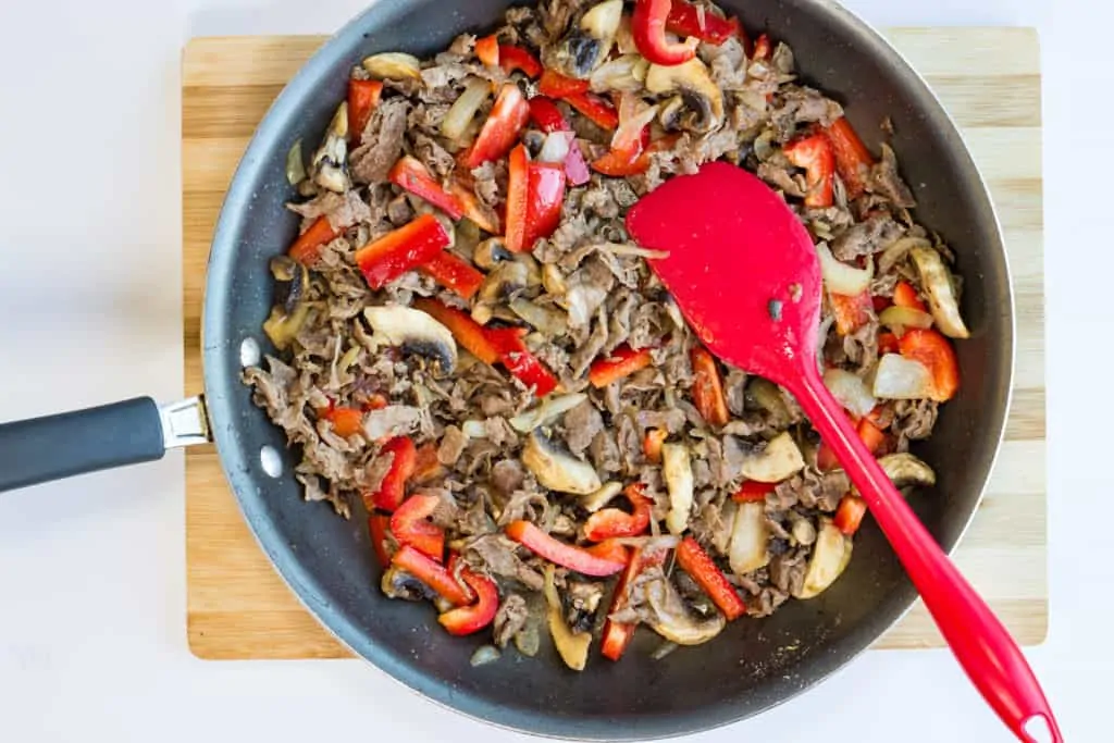red bell peppers added to cooked beef, onions, and mushrooms in a skillet