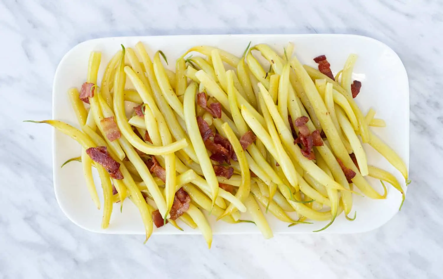 yellow string beans with bacon on a rectangular plate
