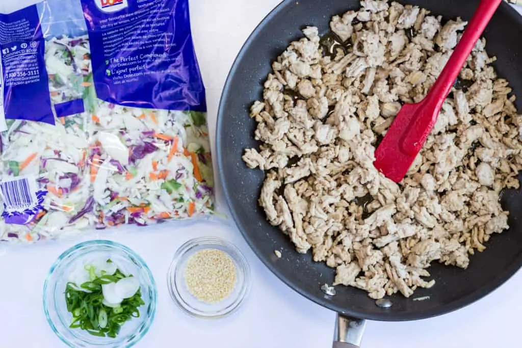 Keto Egg Roll in a Bowl cooked pork in a skillet with other ingredients nearby