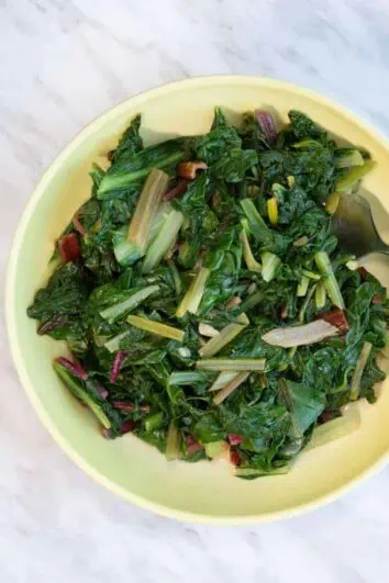 garlicky swiss chard in a yellow serving dish with serving fork