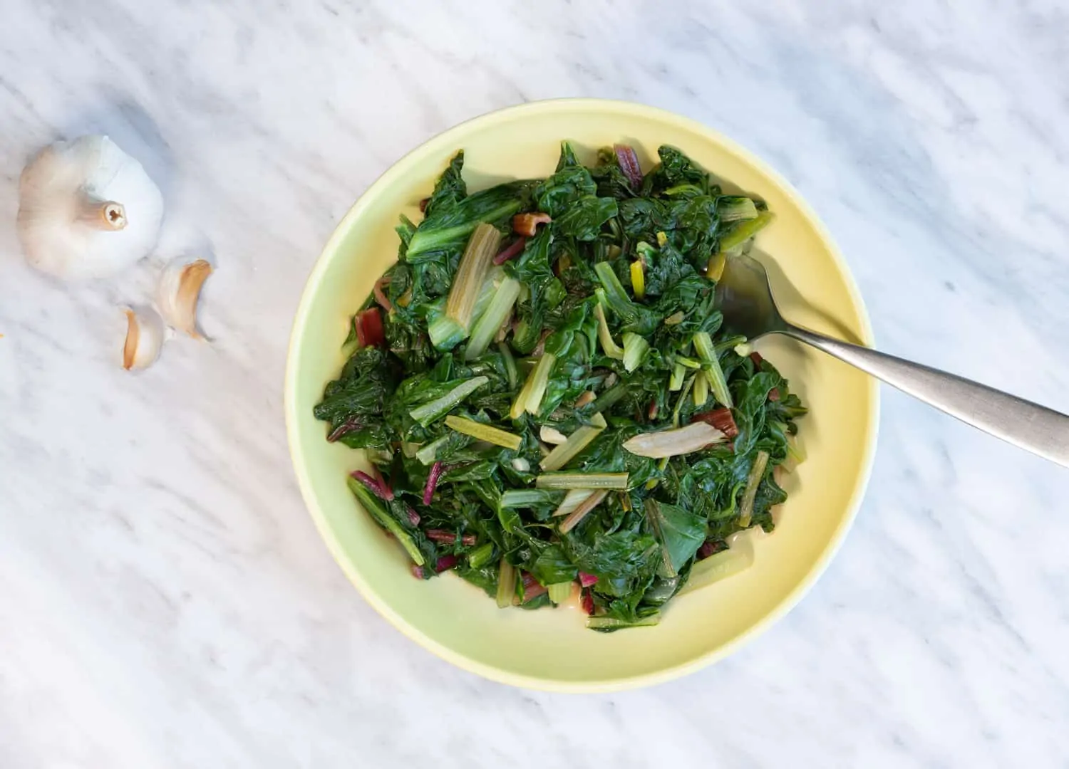 garlicky swiss chard in a yellow serving dish with serving fork