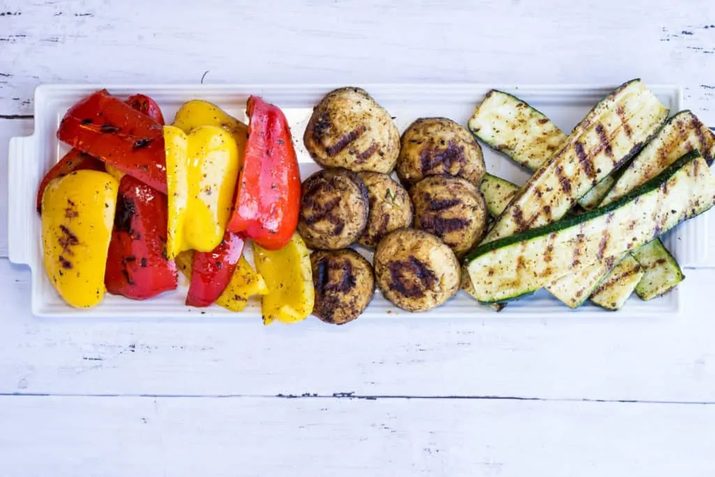 Grilled red and yellow peppers, mushrooms, and zucchini on a platter.