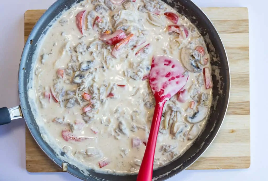 cream added to skillet with philly cheesesteak casserole ingredients