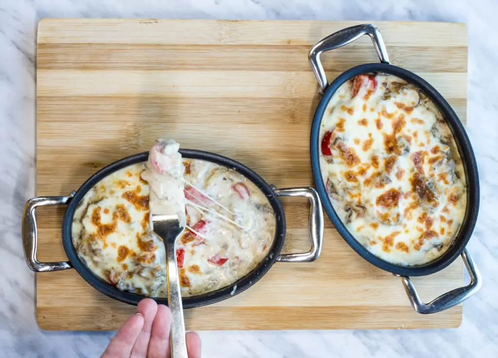 two individual casserole dishes with philly cheesesteak casserole and topped with bubbly cheese