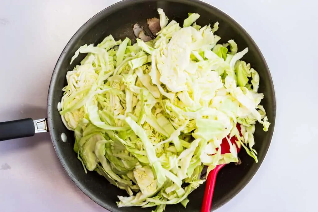 Add raw cabbage to the cooked bacon and garlic.