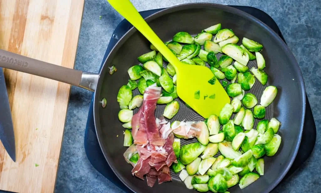Brussels sprouts, garlic and prosciutto in a pan.
