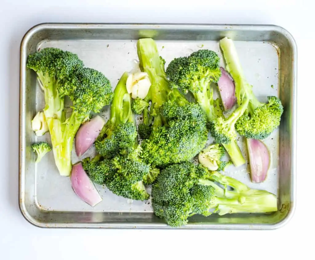 Chopped broccoli, shallot, and garlic drizzled with olive oil and butter on sheet pan.