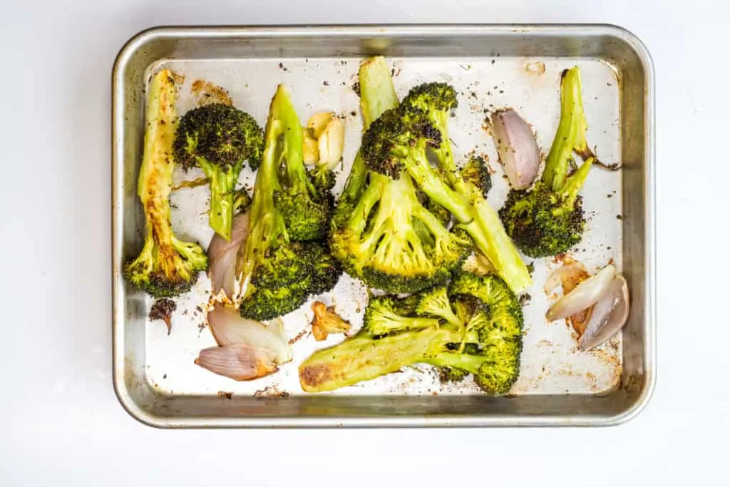 Roasted broccoli, garlic, and shallot on a sheet pan for keto Cream of Roasted Broccoli Soup.