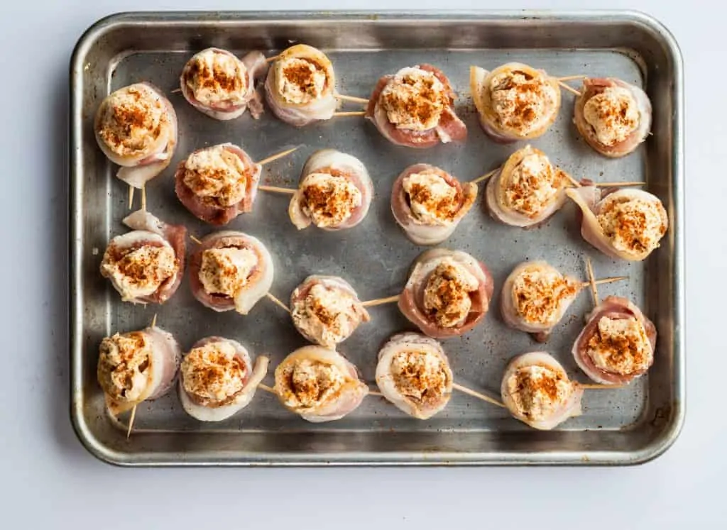 bacon-wrapped pork shots lined up on a baking sheet