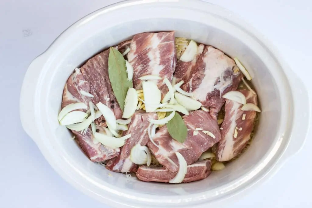 ribs, sauerkraut, bay leaf, onion and garlic in a crock pot ready to cook