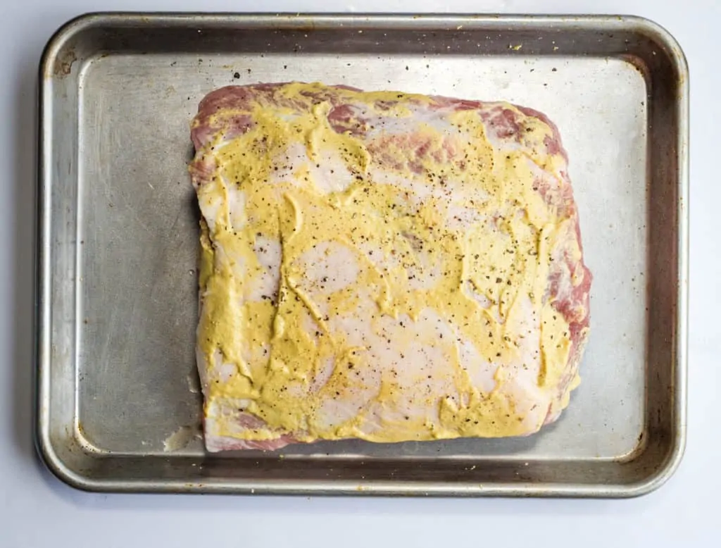 Pork loin on sheet pan brushed with dijon mustard.