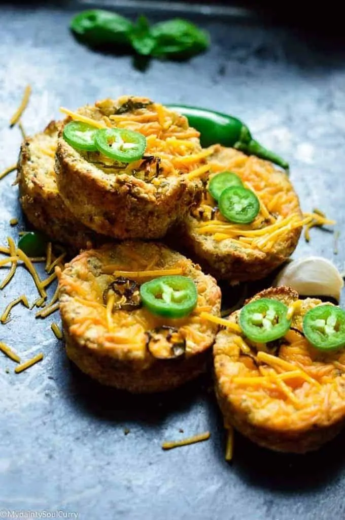 Five Jalapeno-Cheddar Muffins sitting next to a garlic clove, a whole jalapeno and a sprig of basil.