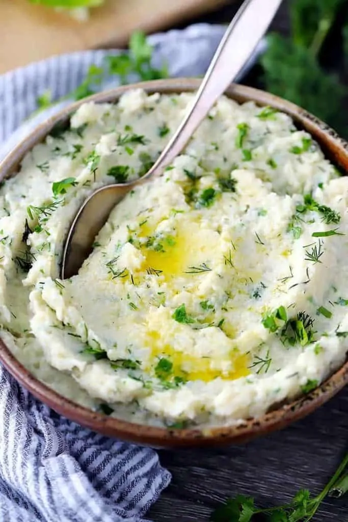 Close-up of a bowl of Mashed Cauliflower with Butter & Herbs with a spoon.