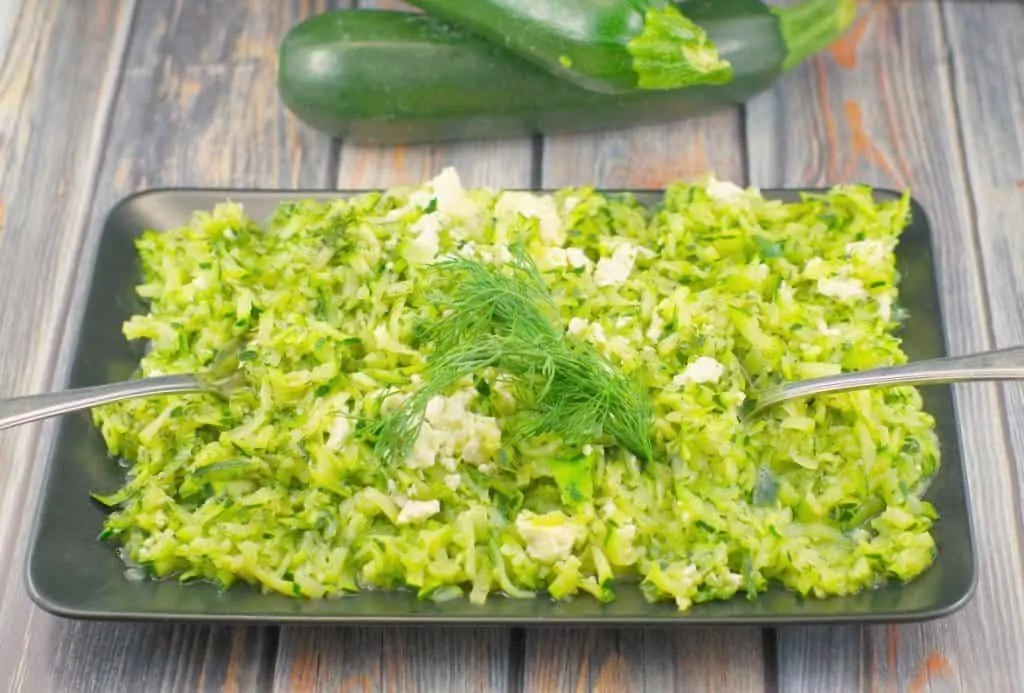 Shredded Zucchini and Feta Sauté on a rectangular black serving dish with a garnish of dill.