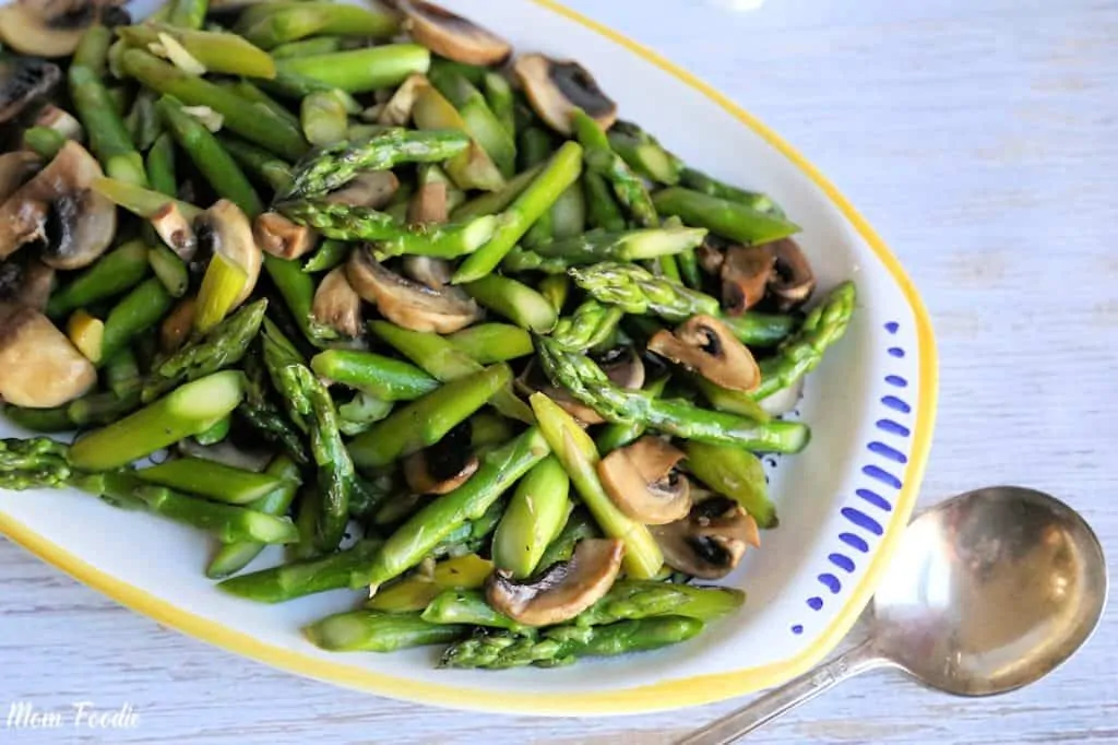 Sauteed Asparagus and Mushrooms in an oval white serving dish with a spoon at the side.