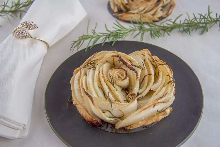 A Turnip Tart on a decorative round plate next to a sprig of rosemary and a fancy napkin.