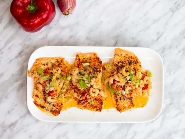 Three keto cajun salmon filets with shrimp and cream sauce on a serving plate