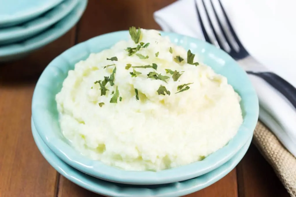 Creamy Mashed Cauliflower in a light blue bowl next to a fork and napkin.