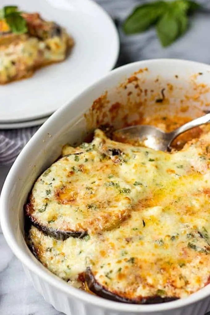 A spoon serving Eggplant Gratin with Feta Cheese onto round white plates.