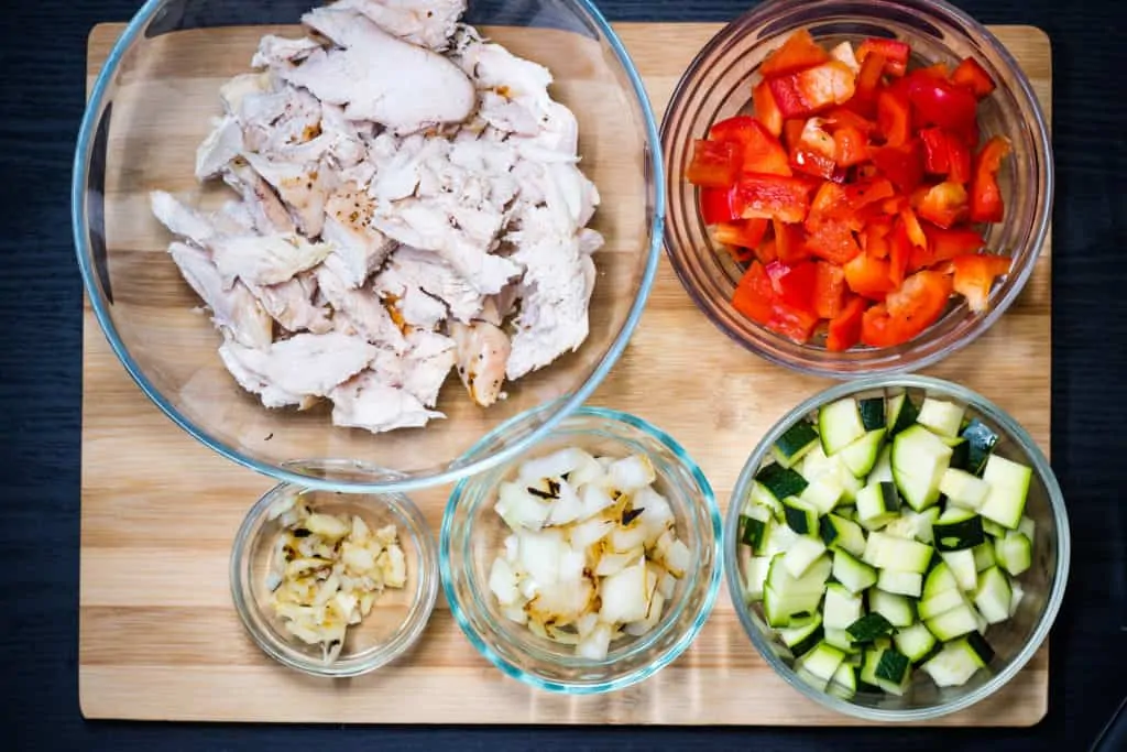 Turkey, pepper, zucchini, onion and garlic prepped in bowls on a cutting board