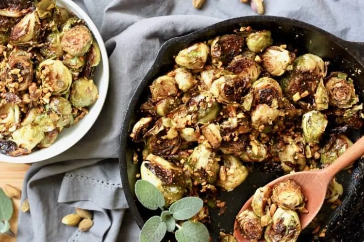 A wooden spoon serving Roasted Brussels Sprouts with Pistachio-Sage Relish into a bowl.