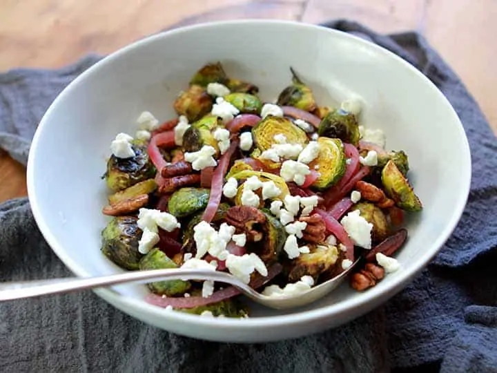 Roasted Garlic Brussels Sprouts with Red Pepper and Parmesan Cheese in a white bowl with a spoon.